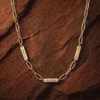 JUNE ELLE gold engraved tag name necklace with Isabella, Oliver and 06.21.2024 on paperclip chain front view on chocolate textured background