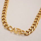 Close-up of JUNE ELLE chunky gold curb chain necklace with personalized AR name pendant.