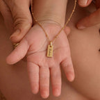 JUNE ELLE Gold Engraved Bar Necklace resting on a baby's hand