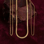 JUNE ELLE gold herringbone custom engraved name necklace with two chain necklaces laid on red gemstone on burgundy velvet background
