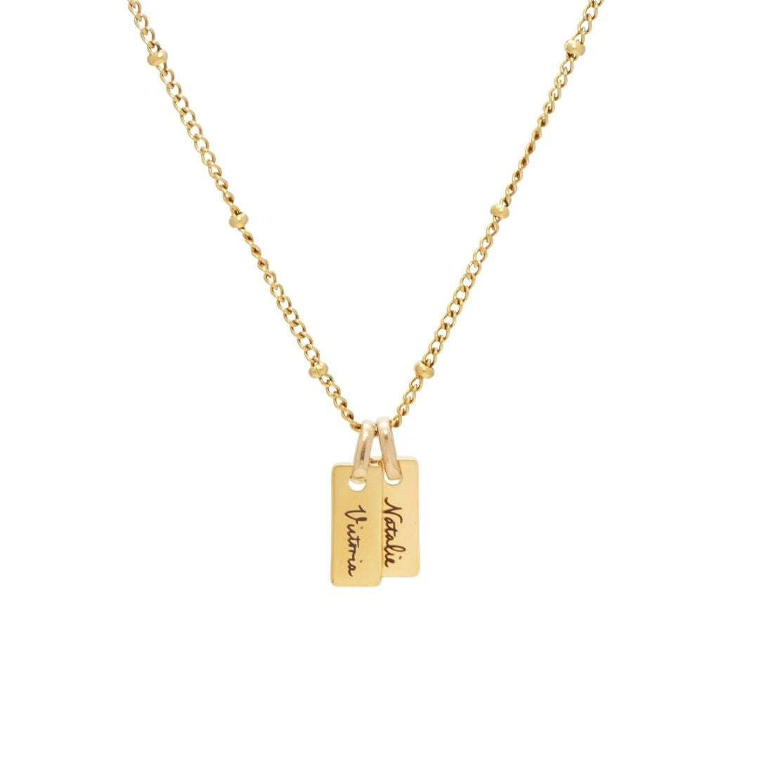 JUNE ELLE Gold Engraved Bar Necklace featuring two personalized nameplates, 'Victoria' and 'Natalie', on a satellite chain.