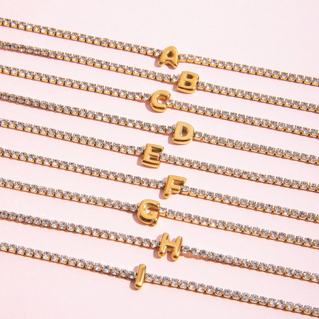 JUNE ELLE gold initial tennis bracelet featuring letters A to I close-up detail view on pink background