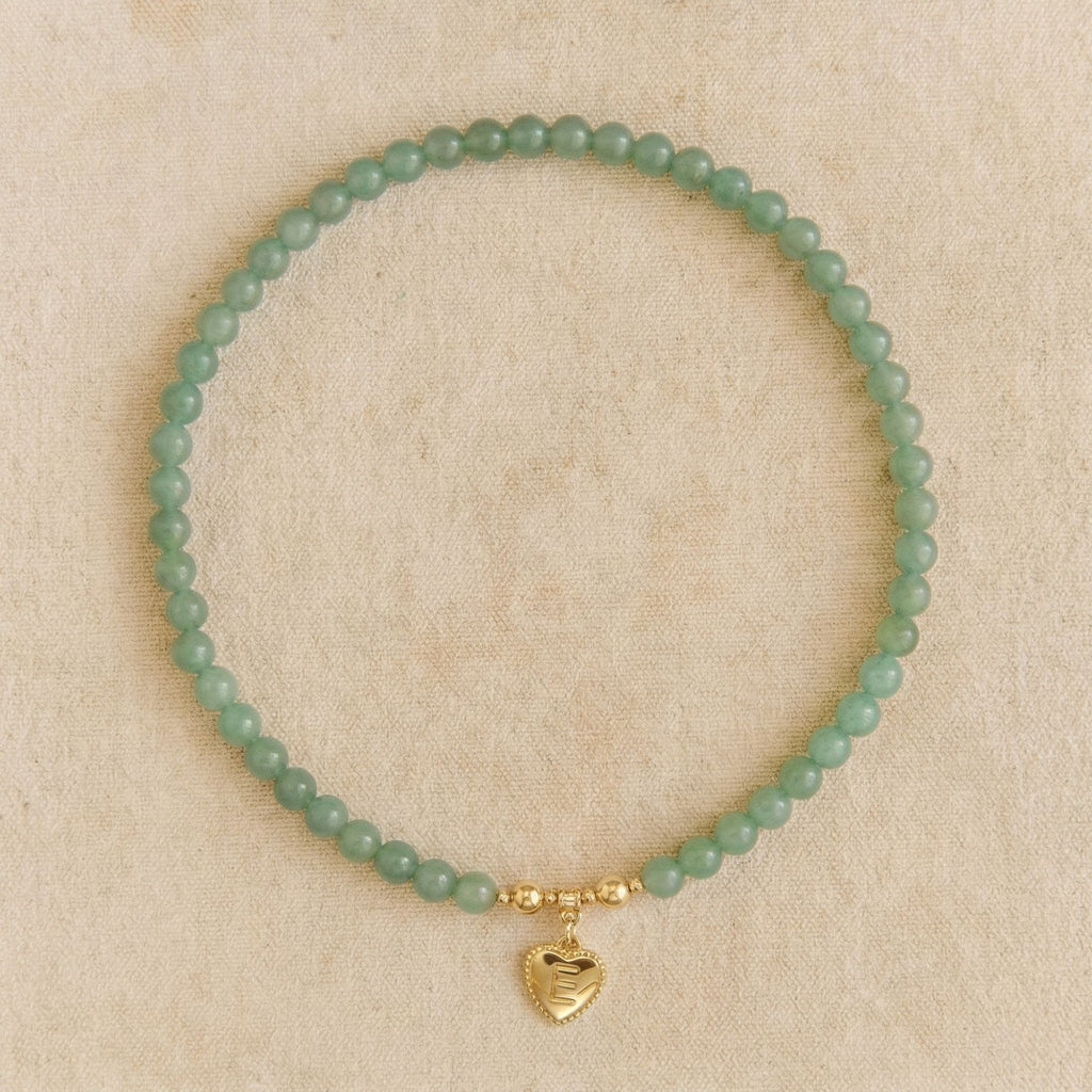 Flat lay of the JUNE ELLE MagMix interchangeable necklace, combining a Green Aventurine bead base chain with a custom gold heart initial charm centerpiece connected by gold magnetic clasps, resting on a textured beige fabric background.