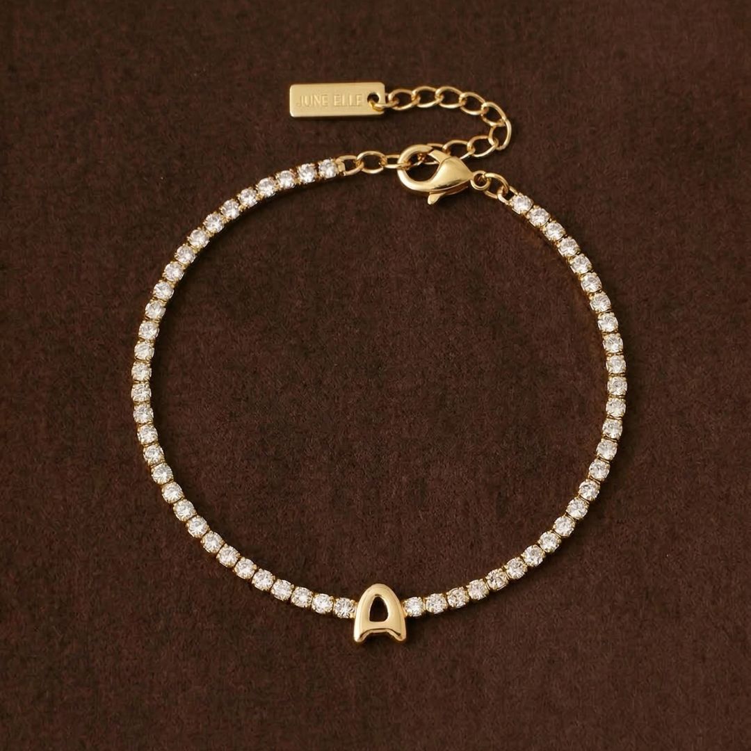 JUNE ELLE gold initial tennis bracelet with letter A arranged in a perfect circle on chocolate fabric background front view