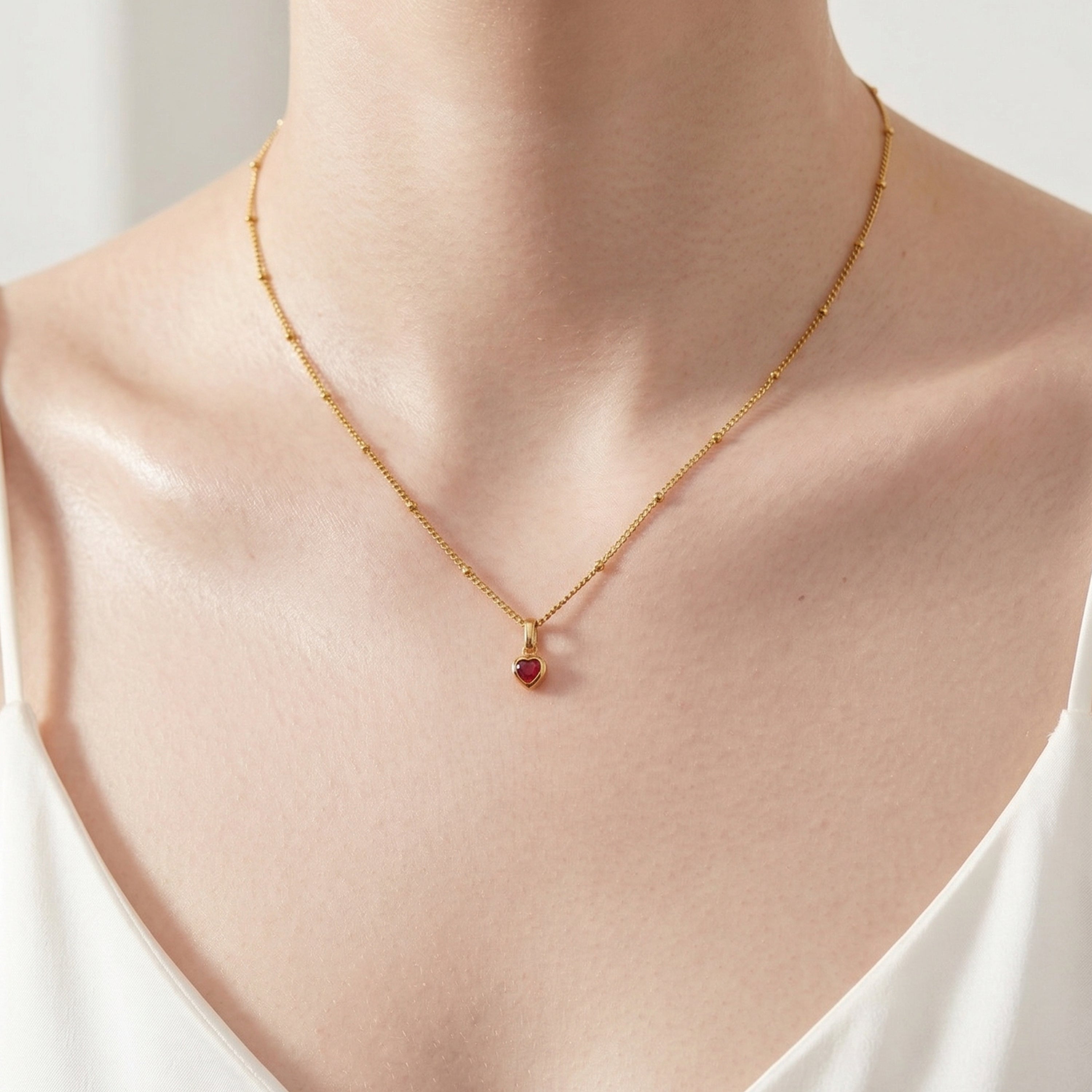 Model wearing UNE ELLE gold heart birthstone charm necklace in 18K gold plated finish