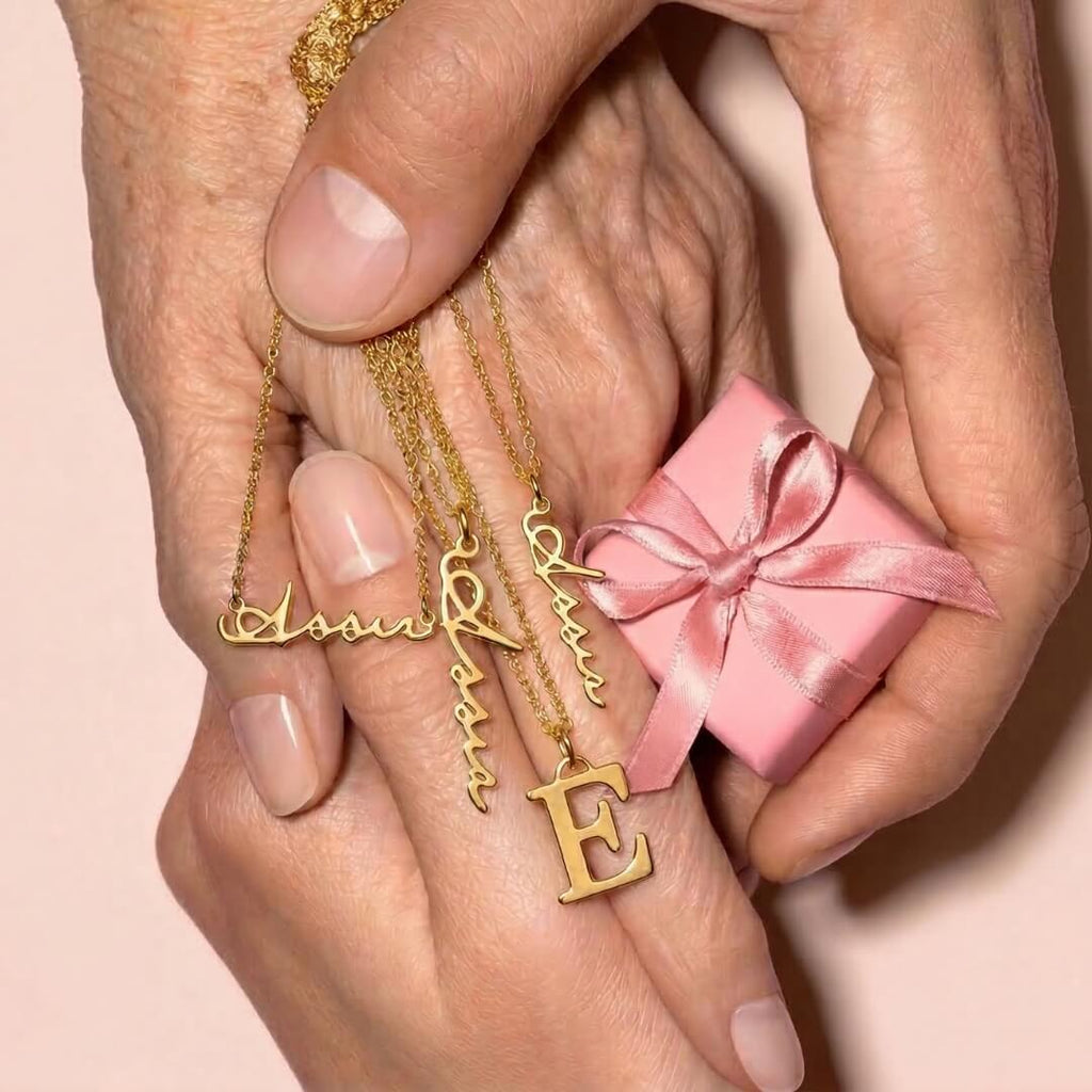 Hands holding pink gift box and JUNE ELLE 18K gold plated E initial pendant with cursive name necklaces laid across clasped palms, styled scene