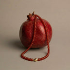 JUNE ELLE MagMix Carnelian Bead Necklace with a central gold magnetic clasp, gracefully draped over a ripe, dark red pomegranate on a neutral background.