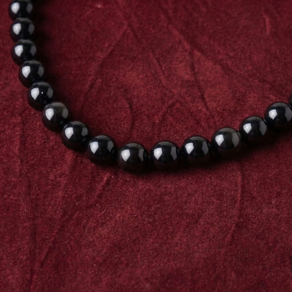 Close-up of JUNE ELLE MagMix black obsidian bead necklace on deep red textured fabric.