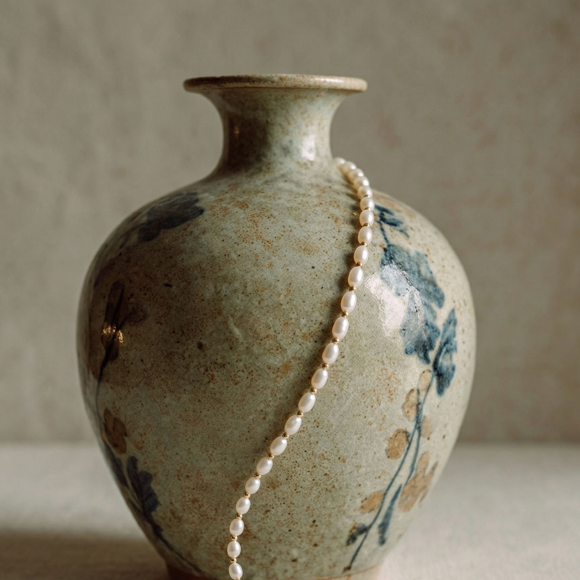 Elegant still life of the JUNE ELLE MagMix seed freshwater pearl necklace, gracefully draped over a rustic floral ceramic vase.