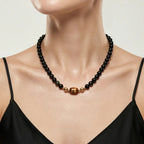 Model wearing the JUNE ELLE MagMix interchangeable necklace, combining a black obsidian bead base chain with a Tiger’s Eye barrel centerpiece connected by gold magnetic clasps.