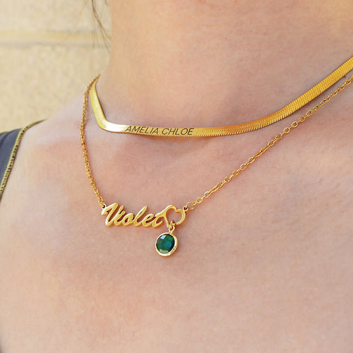 layered gold necklaces featuring birthstone name necklace with Violet and round birthstone paired with engraved herringbone necklace worn on model